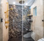 This gold-speckled granite accent wall along with body sprays and ceiling rain head, shower you with luxury.